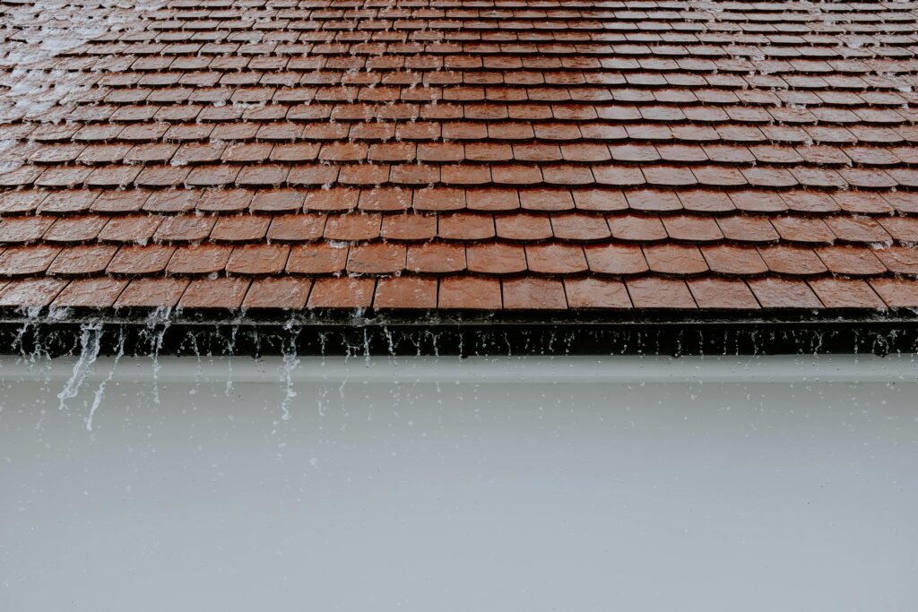 pexels-photo-2663254-2663254 Brown roof tiles with rainwater cascading down, showcasing architectural texture and detail.