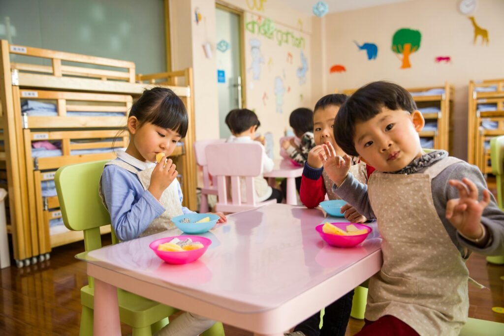 pexels-photo-1001914-1001914 Kids seated around a table in a colorful classroom, eating snacks happily.